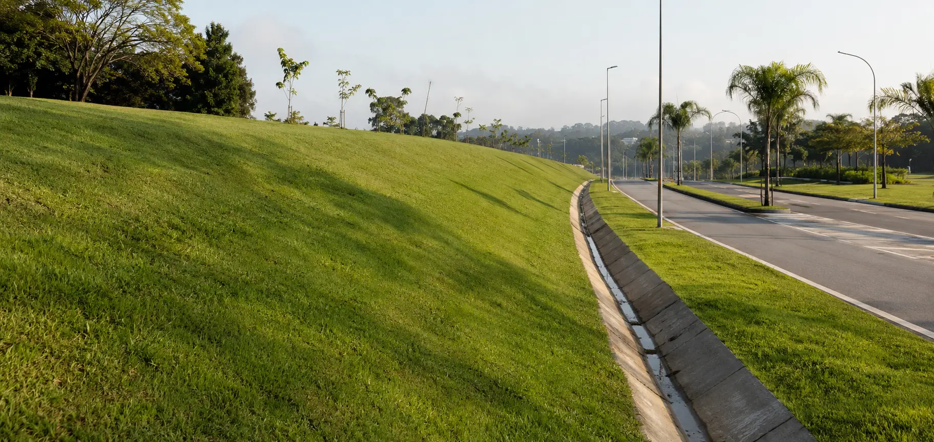 Talude gramado com canal de drenagem ao lado de avenida arborizada